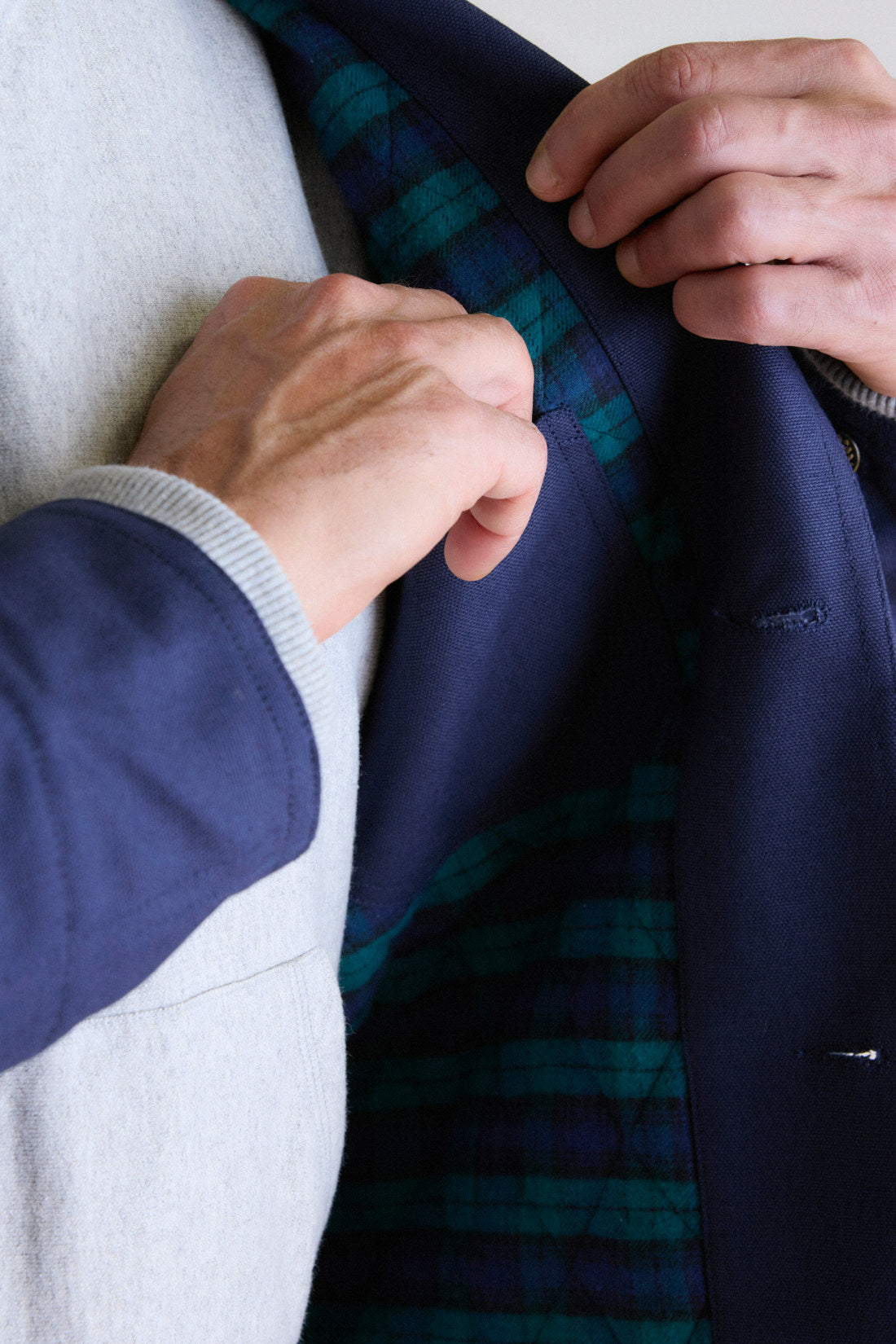 Hands fastening a navy duck canvas chore coat, the weave of the cloth and the cuff visible up close