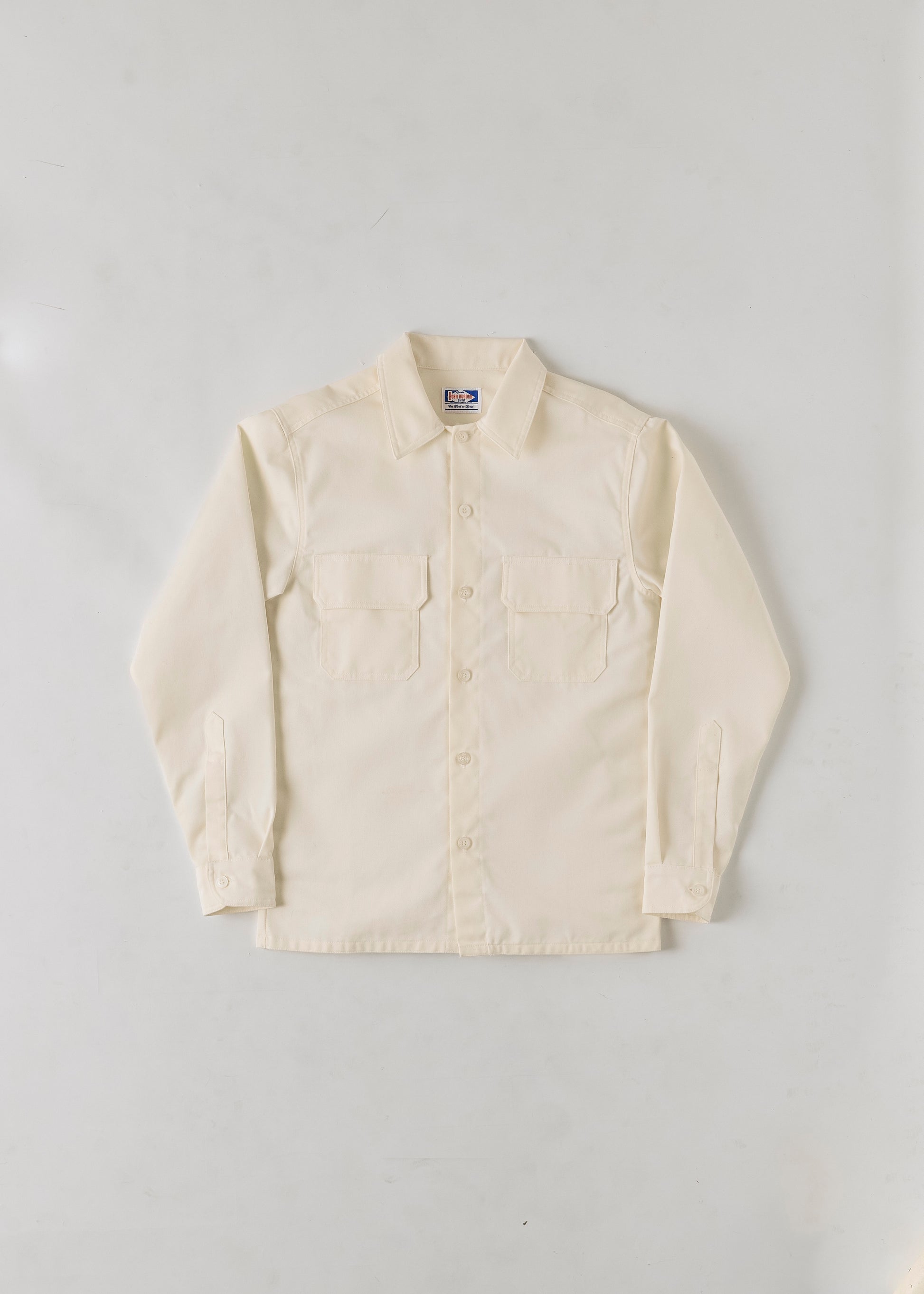 Flat lay of a cream coloured button up collared long sleeve shirt on a grey background.