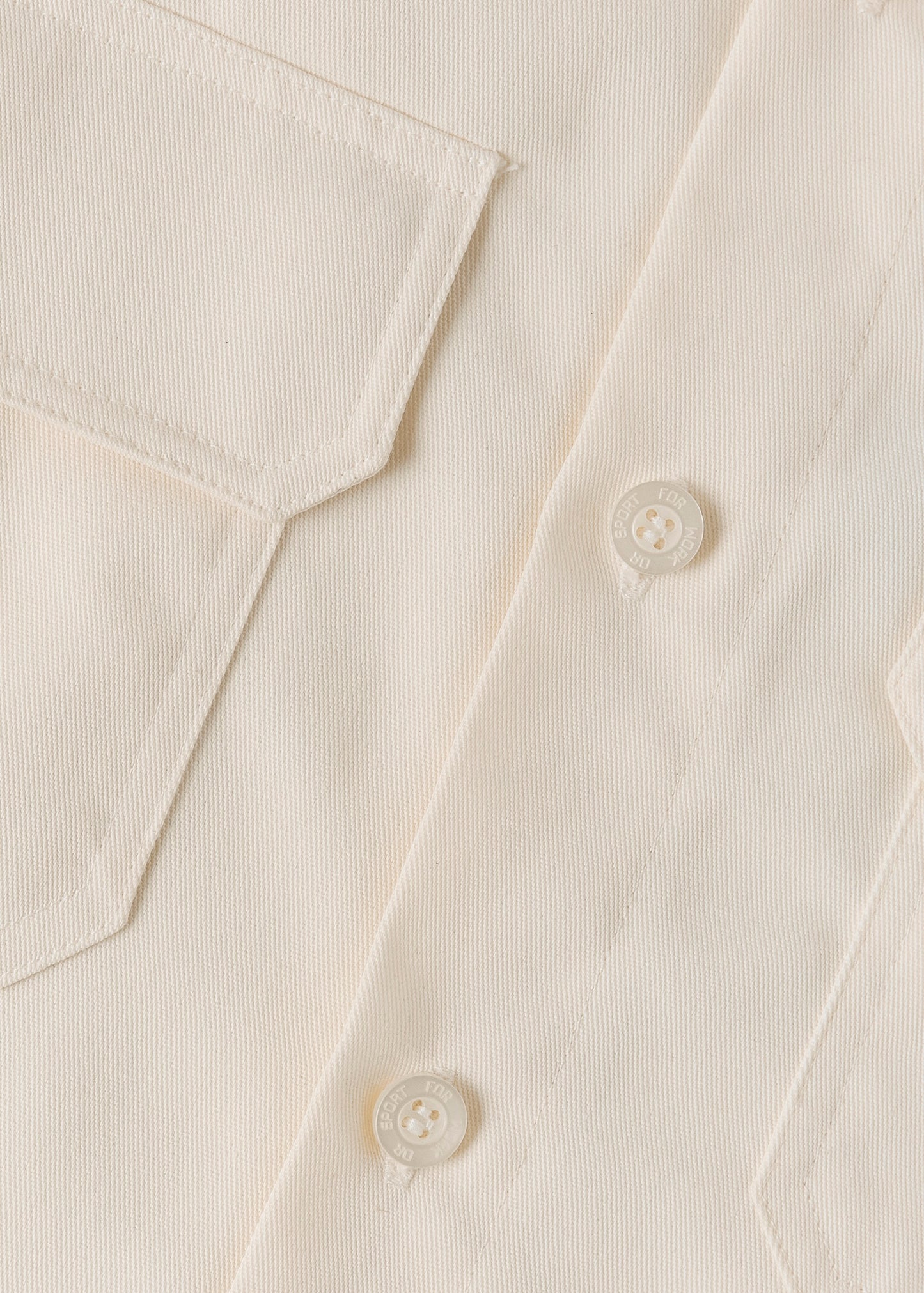 Close up of a cream coloured button on a cream coloured shirt.