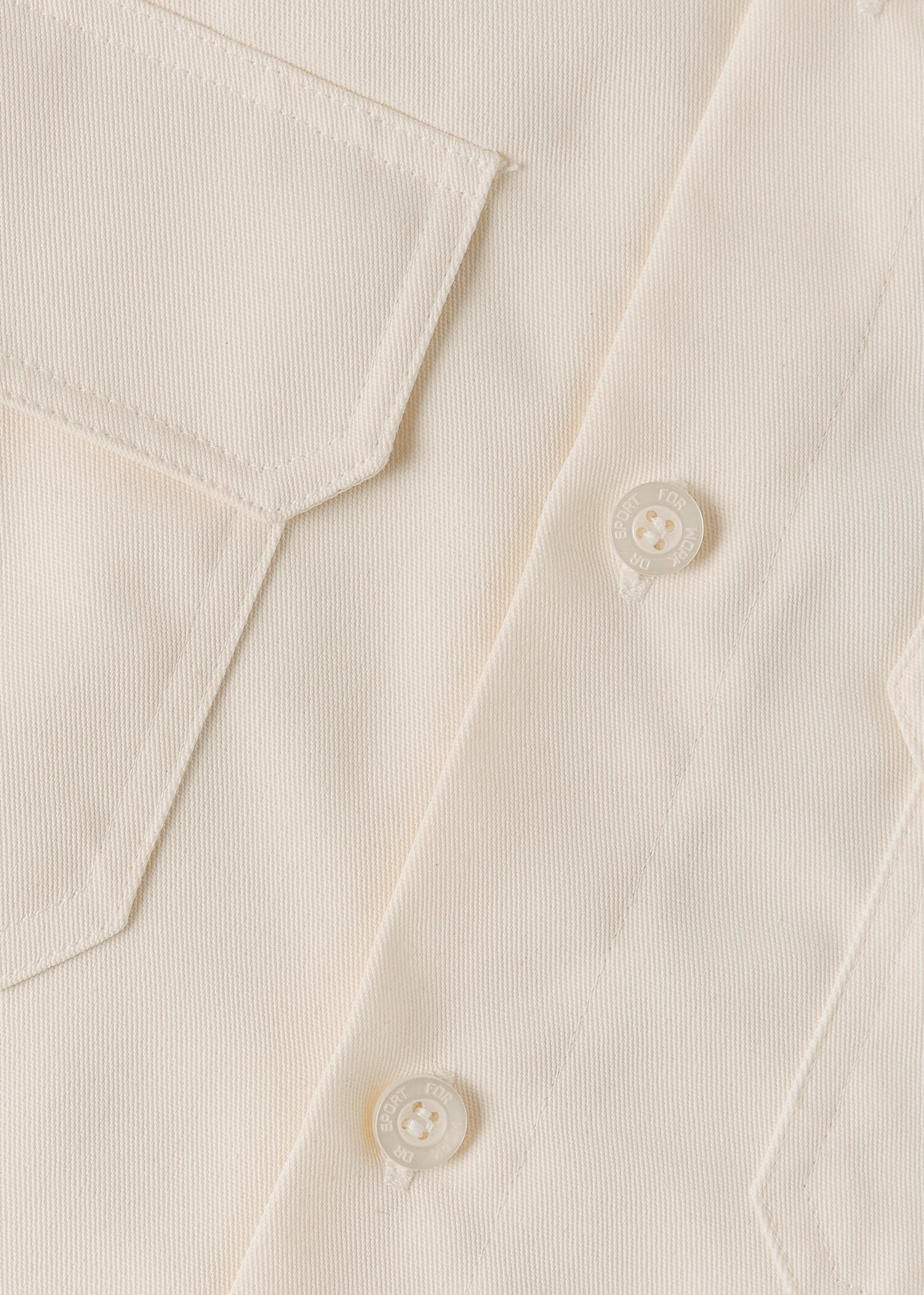 Close up of a cream coloured button on a cream coloured shirt.