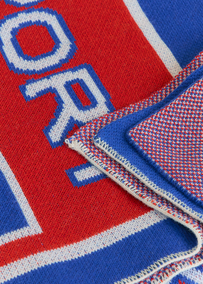 Close up of red and blue knitted blanket showing finished edges and knit texture. 
